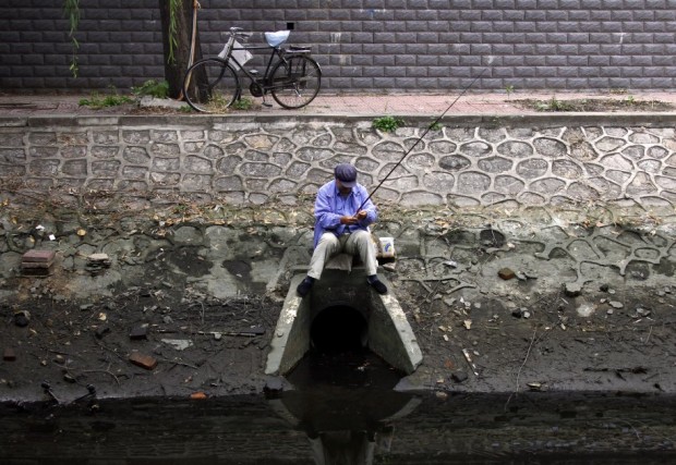 a-fisherman-sits-on-top-of-a-drain-at-a-polluted-canal-in-central-beijing