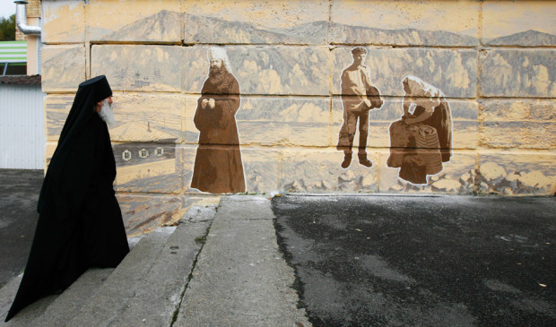 Ο 74χρονος ορθόδοξος μοναχός, πατέρας Ιωακείμ, κοιτάζει γκράφιτι του δρόμου, στο οποίο απεικονίζεται ορθόδοξος μοναχός μαζί με τυπικούς χαρακτήρες της Σιβηρίας του 19ου αιώνα στην πόλη Ντιβνογκόρσκ, λίγο έξω από το Κρασνογιάρσκ της Σιβηρίας, στις 30 Σεπτεμβρίου 2013. Πηγή: Reuters