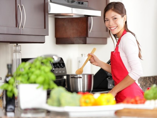Cooking woman in kitchen stirring in pot making food for dinner. Young housewife smiling happy looking at camera. Mixed-race Caucasian / Asian chinese woman in her twenties.