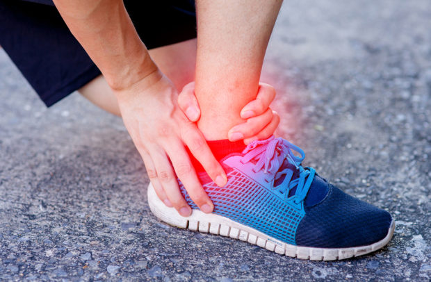 Runner touching painful twisted or broken ankle. Athlete runner training accident. Sport running ankle sprain.