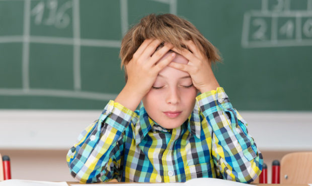 Young boy concentrating on his schoolwork sitting at his desk in the classroom with his head in his hands reading his class notes