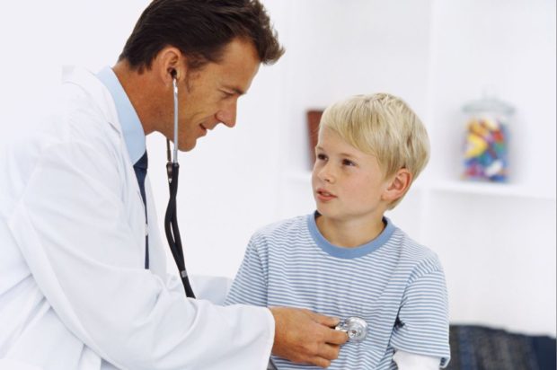 Side profile of a male doctor checking a young boy's (8-10) chest with a stethoscope