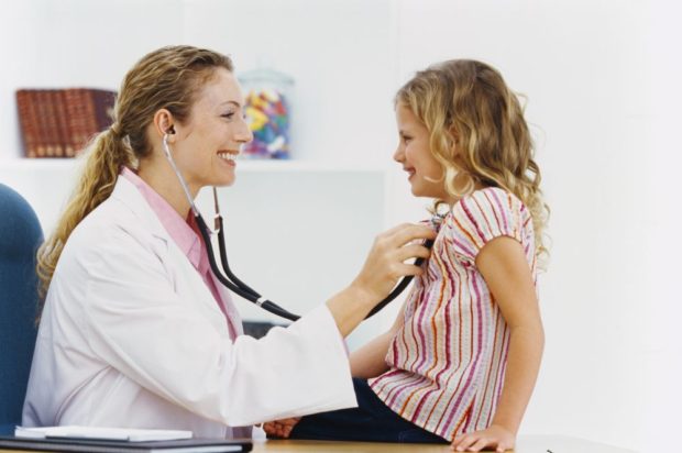 Side profile of a female doctor checking a young girl's (6-8) chest with a stethoscope