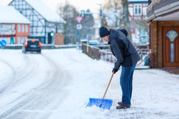 Man with snow shovel cleans sidewalks in winter. Winter time in Europe. Young man in warm winter clothes